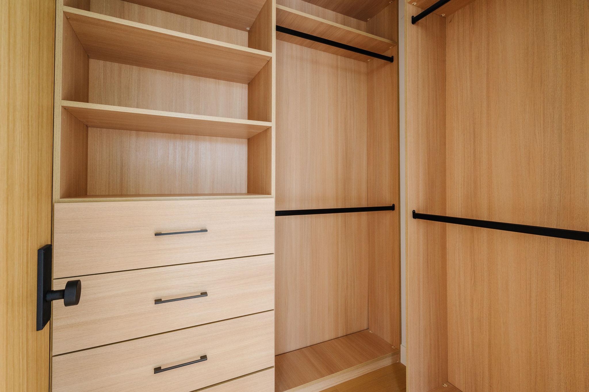 Built-in light oak closet storage with open shelving and black hardware